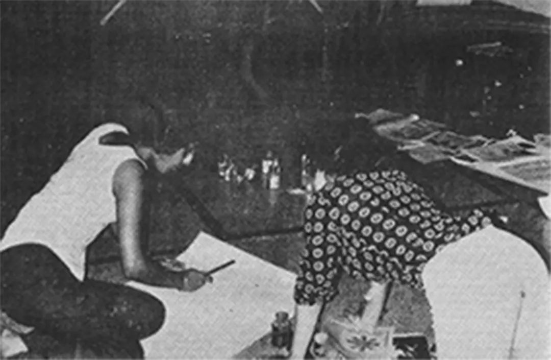 Two people bent over a painting on the floor