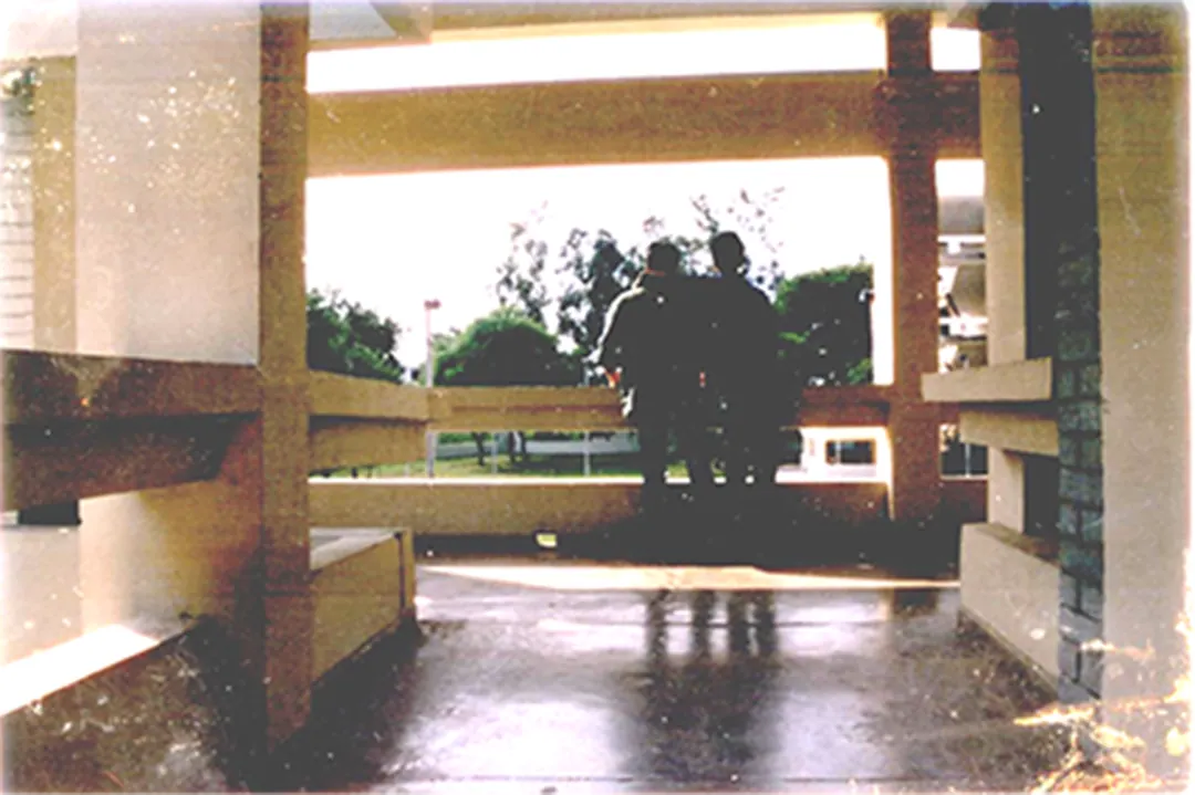 Two people sit in a campus corridor, the light behind them