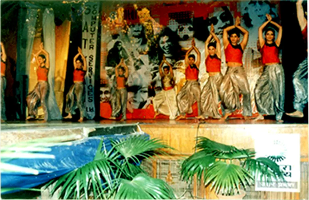 A dance group in red on a stage decorated with palms